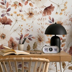 Puede incluir: Un escritorio de oficina en casa con un papel tapiz floral con flores de acuarela en tonos marrones, blancos y amarillos. El escritorio tiene una tapa de madera y una l&aacute;mpara negra con un reloj blanco que marca "S&Aacute;B 10".