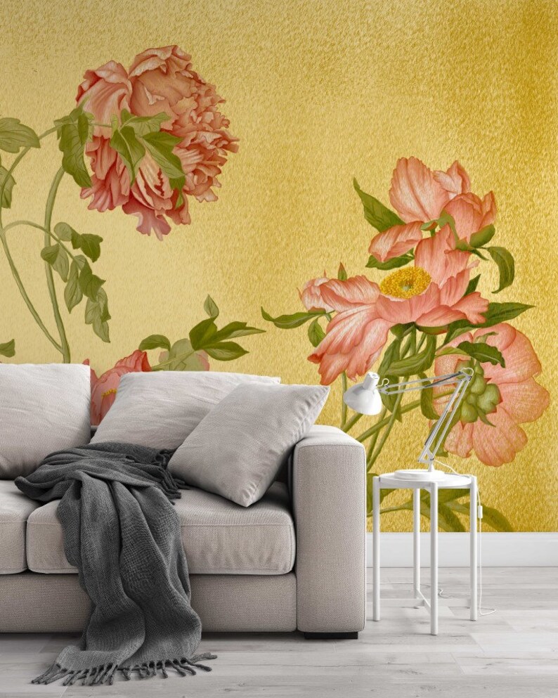 May include: A white sofa with a grey throw blanket in front of a wall with a floral pattern. The floral pattern features pink peonies on a yellow background.