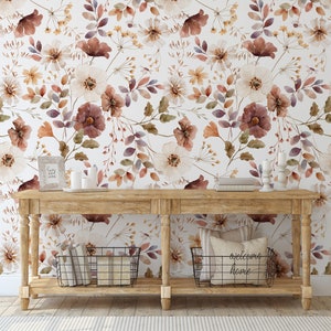 Puede incluir: Una consola de madera con un fondo de papel tapiz floral blanco. La mesa tiene dos estantes y est&aacute; decorada con velas, libros y una cesta. El papel tapiz presenta un patr&oacute;n floral de acuarela en tonos marrones, blancos y morados.