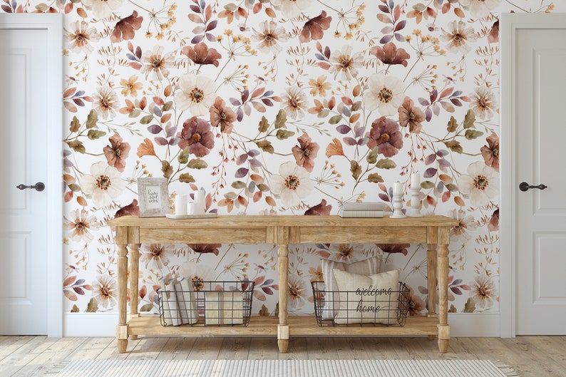Puede incluir: Una consola de madera con un fondo de papel tapiz floral blanco. La mesa tiene dos estantes y est&aacute; decorada con velas, libros y una cesta. El papel tapiz presenta un patr&oacute;n floral de acuarela en tonos marrones, blancos y morados.
