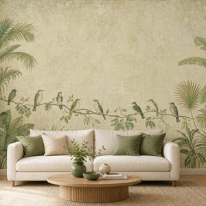 May include: A beige wall mural featuring a horizontal branch with green tropical leaves and several small birds perched along it. The mural has a textured, weathered appearance and is positioned behind a white sofa with green and beige pillows.