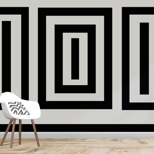 Puede incluir: Tres cuadrados negros enmarcados con l&iacute;neas negras conc&eacute;ntricas en una pared blanca. Los cuadrados est&aacute;n dispuestos en una fila. Una silla blanca con un coj&iacute;n de patr&oacute;n blanco y negro se encuentra frente a la pared.