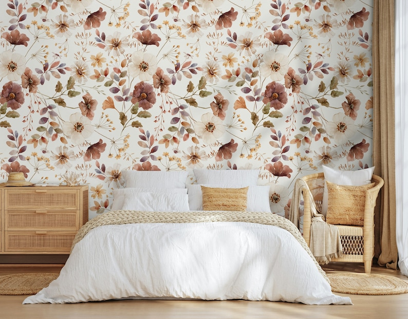 Puede incluir: Una cama blanca con una funda n&oacute;rdica blanca y una manta de punto beige. La cama est&aacute; frente a una pared con un papel tapiz floral con un patr&oacute;n de flores marrones, blancas y moradas. Una silla de mimbre beige con un coj&iacute;n beige est&aacute; a la derecha de la cama.