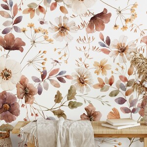 Puede incluir: Un papel tapiz floral de acuarela con fondo blanco y un patr&oacute;n de flores y hojas marrones, naranjas y moradas. El papel tapiz se muestra en un ambiente de dormitorio con una cama, un espejo y una mesita de noche.