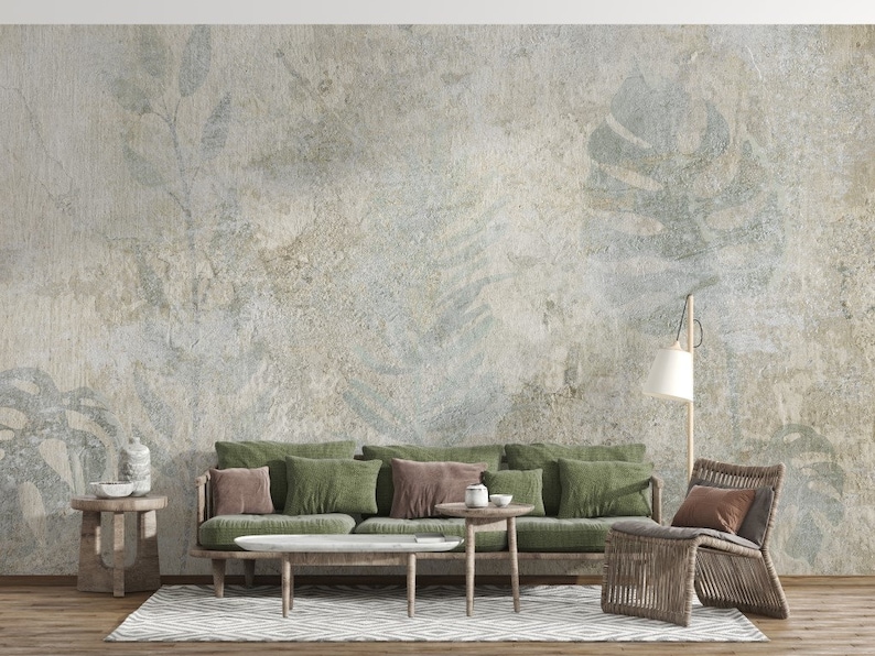 Puede incluir: Un dise&ntilde;o de interior de sala de estar con un sof&aacute; verde, dos mesas auxiliares, una l&aacute;mpara de pie y una silla de mimbre. La pared est&aacute; decorada con un papel tapiz texturizado con un sutil patr&oacute;n de hojas en tonos verdes y grises.