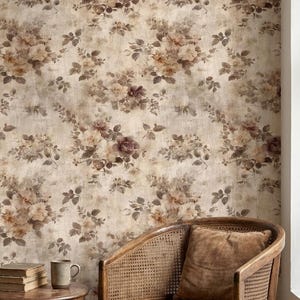 Puede incluir: Papel pintado floral de estilo vintage. El diseño presenta racimos de rosas en tonos marrón, beige y púrpura sobre un fondo texturizado. Una silla de madera con un cojín y una pequeña mesa con libros y una taza están en primer plano.