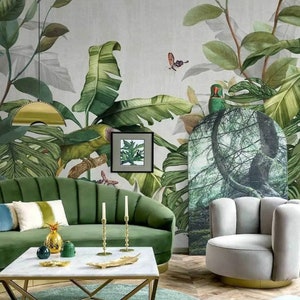 Puede incluir: Un dise&ntilde;o de interior de sala de estar con un sof&aacute; de terciopelo verde, una mesa de caf&eacute; blanca, un sill&oacute;n gris y un papel tapiz tropical con hojas verdes y un loro.
