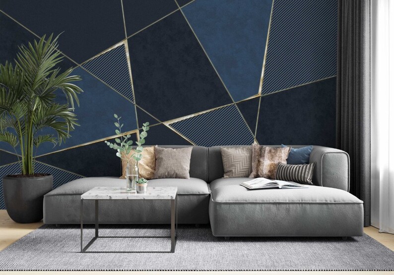 May include: A gray sectional sofa with pillows sits in front of a wall with a geometric pattern of gold lines on a dark blue background.