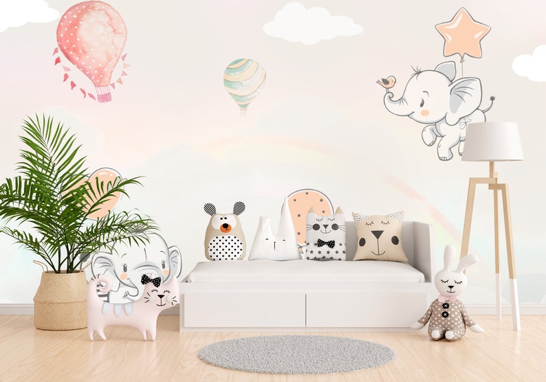 May include: A white couch with a rainbow design on the wall behind it. There are several stuffed animals on the couch, including a cat, a bear, a rabbit, and an elephant. There is also a plant in a woven basket in the corner of the room.