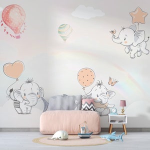 May include: A nursery room with a pink couch and a white wall with a rainbow, clouds, and cute elephant illustrations. The elephants are holding balloons in the shape of hearts and stars.