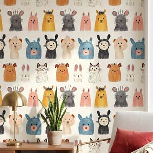 以下が含まれることがあります： さまざまな色の漫画の動物の顔が繰り返されるパターンの壁紙。動物には、クマ、ウサギ、猫、ネズミが含まれ、青、ピンク、黄色、黒のアクセントがあります。壁紙は、木製のキャビネット、ランプ、椅子のある壁にあります。