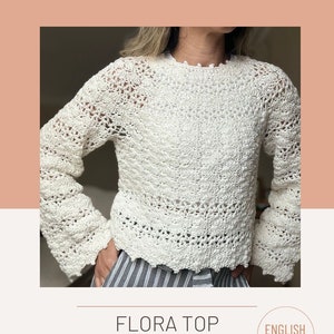 Peut inclure: Un haut en crochet blanc avec un motif en dentelle. Le haut a des manches longues et un col rond. Le modèle s'appelle "Flora Top Crochet Pattern" et est disponible en anglais.