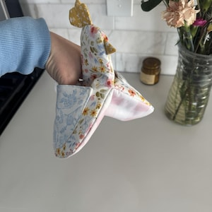 K&ouml;nnte beinhalten: Ein handgemachter Ofenhandschuh in Form eines Huhns. Der Handschuh hat einen gelben Kamm und Stoff mit Blumenmuster in Wei&szlig;, Gelb und Rosa. Die Innenseite ist mit einem rosa-wei&szlig; gestreiften Stoff gef&uuml;ttert, und die Manschette hat ein blaues Blumenmuster.
