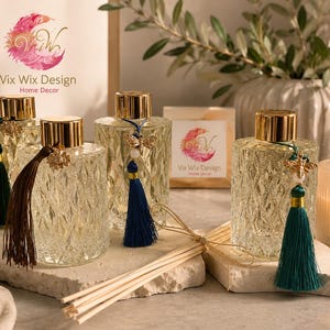 May include: Four clear glass reed diffuser bottles with a diamond-cut texture and gold-tone caps. Each bottle features a decorative charm of a bee and a hanging tassel in dark green, brown, navy blue, or teal. Bundles of wooden reeds are included.