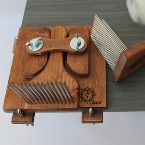 Può includere: Uno strumento di cardatura della lana in legno con un pettine in metallo e un manico in legno. Lo strumento è montato su una base in legno con una vite in metallo. La base ha un logo con il testo "Cirao".