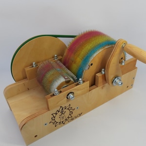 Puede incluir: Un torno de hilar de madera con dos rodillos de cepillo de colores y una manija verde. La rueda está etiquetada como "Sunray".
