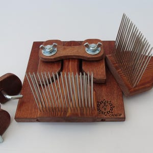 May include: A wooden wool carding tool with two sets of metal teeth. The tool is made of dark brown wood and has a handle on the right side. The tool is used to card wool fibres, which is a process of aligning the fibres to make them smoother and more even.
