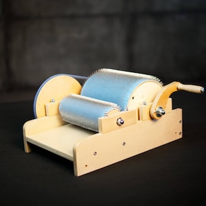 Puede incluir: Un torno de hilar de madera con un rodillo de cepillo azul y un mango de madera. El torno est&aacute; sobre una superficie negra.