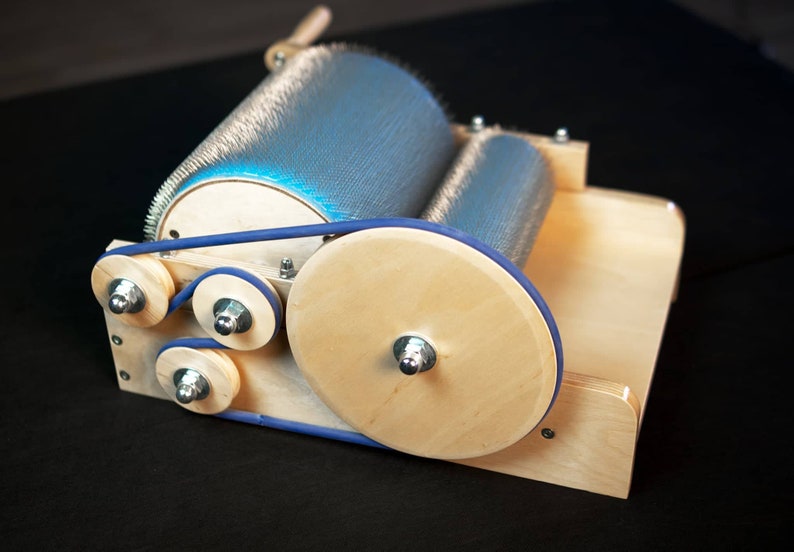 Puede incluir: Un torno de hilar de madera con una correa de goma azul y un rodillo de aguja de metal. El torno est&aacute; hecho de madera clara y tiene un acabado natural.