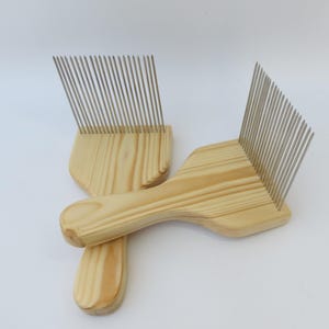 May include: Two wooden combs with metal teeth, used for carding wool or other fibers. The combs are made of light wood and have a natural finish.