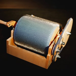 Puede incluir: Una rueca de madera con un cepillo de metal y una manivela. La rueca est&aacute; hecha de madera clara y tiene una mancha marr&oacute;n oscura. El cepillo est&aacute; hecho de metal y tiene un acabado plateado. La manivela est&aacute; hecha de madera y tiene un acabado marr&oacute;n claro.