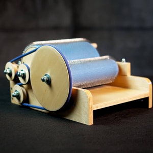 Puede incluir: Un torno de hilar de madera con un rodillo azul y plateado. El torno tiene una base de madera y una correa azul.