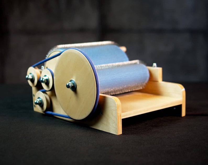 Puede incluir: Un torno de hilar de madera con un rodillo azul y plateado. El torno tiene una base de madera y una correa azul.