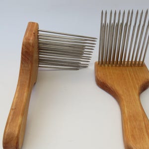 Op de afbeelding: Twee wollen kammen van hout met metalen tanden. De kammen zijn bruin en hebben een natuurlijke houten afwerking. De tanden zijn zilverkleurig en zijn in een rij gerangschikt.