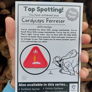 Può includere: Una carta bianca con il testo "Top Spotting! Cordyceps Ferreter skills badge." La carta presenta una toppa triangolare rossa con un disegno giallo e bianco e un'illustrazione in bianco e nero di una persona. La carta elenca anche altri badge.