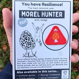 Puede incluir: Una tarjeta blanca con el texto "You have Resilience! You have achieved your MOREL HUNTER skills badge" y un parche triangular rojo con un diseño de hongo blanco. El texto "Yes!" está en un bocadillo de diálogo. La tarjeta también incluye el texto "42/150" y una descripción de las habilidades necesarias para ser un cazador de morillas.