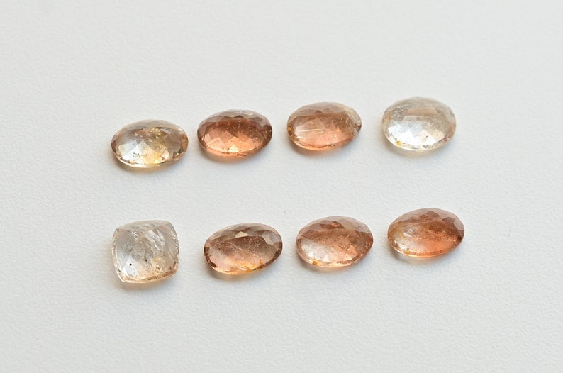 May include: Eight faceted gemstones in various shades of brown and clear. The gemstones are oval and rectangular in shape.