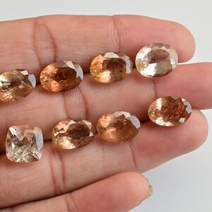 May include: Eight faceted gemstones in various shades of brown, including a square-shaped stone, displayed on a hand.
