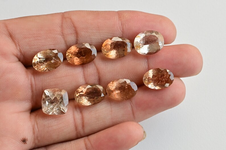 May include: Eight faceted gemstones in various shades of brown, including a square-shaped stone, displayed on a hand.