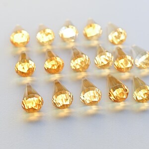 Puede incluir: Una colecci&oacute;n de 18 cristales facetados en forma de l&aacute;grima en tonos &aacute;mbar y dorado.