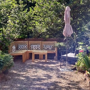 May include: A wooden patio set with three cushioned benches and a small table. The set is in a garden setting with green foliage and a pink parasol.