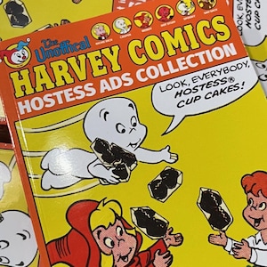 May include: A collection of Harvey Comics Hostess Ads. The cover features cartoon characters with the text "HARVEY COMICS HOSTESS ADS COLLECTION" and "LOOK, EVERYBODY, HOSTESS CUP CAKES!". The image is filled with yellow and orange boxes with cartoon characters and Hostess snacks.