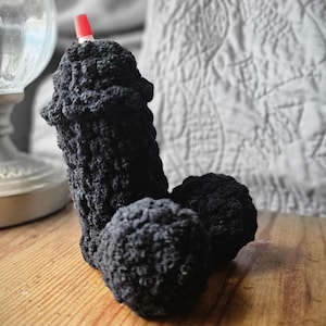 Puede incluir: Una escultura negra y texturizada de ganchillo con un elemento de punta roja en la parte superior. La escultura está sobre una superficie de madera. El fondo está borroso, con una lámpara y una superficie blanca estampada.