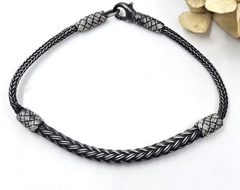 May include: A black braided silver bracelet with a clasp closure. The bracelet has a woven design and is made of sterling silver.