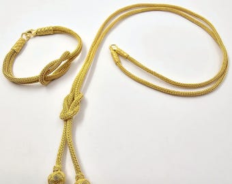 May include: A gold necklace and bracelet set with a knotted design. The necklace has two strands and ends with gold balls. The bracelet is a single strand with a knot in the center.