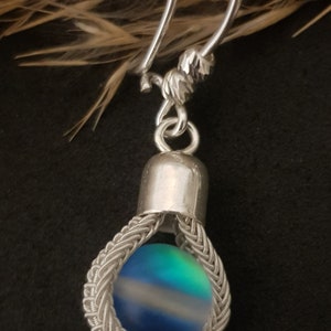 May include: Silver earring featuring a blue, green and white iridescent glass bead enclosed in a silver wire cage.