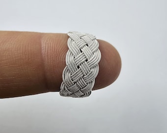 May include: A silver braided ring, woven from multiple strands of metal, is shown on a finger.