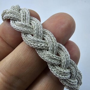May include: A silver braided bracelet with a woven design.