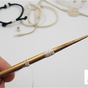 May include: A close-up of a brass tool with a white cord wrapped around it. The tool has a wooden handle and a sharp point. The tool is used for making jewellery.