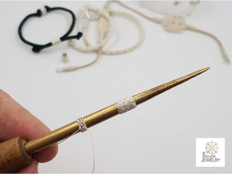 May include: A close-up of a brass tool with a white cord wrapped around it. The tool has a wooden handle and a sharp point. The tool is used for making jewellery.