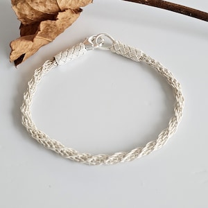 Puede incluir: Un brazalete trenzado de plata con cierre de broche. El brazalete está hecho de un alambre delicado e entrelazado.