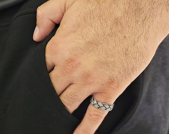 May include: A silver braided ring on a finger.