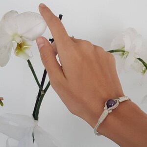 May include: A silver bracelet featuring a purple gemstone at its centre. The bracelet is crafted from wire that is intricately woven to create a delicate design.