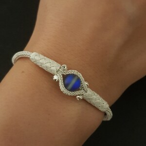 May include: A silver bracelet with a woven design and a blue iridescent stone in the centre.