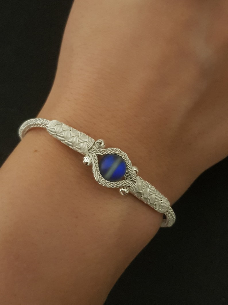 May include: A silver bracelet with a woven design and a blue iridescent stone in the centre.