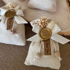 May include: Two small burlap bags with white ribbon bows and gold wax seals. The seals have the words "With Love" and "Thank You" on them. The bags are filled with dried flowers and have wooden beads on the strings.